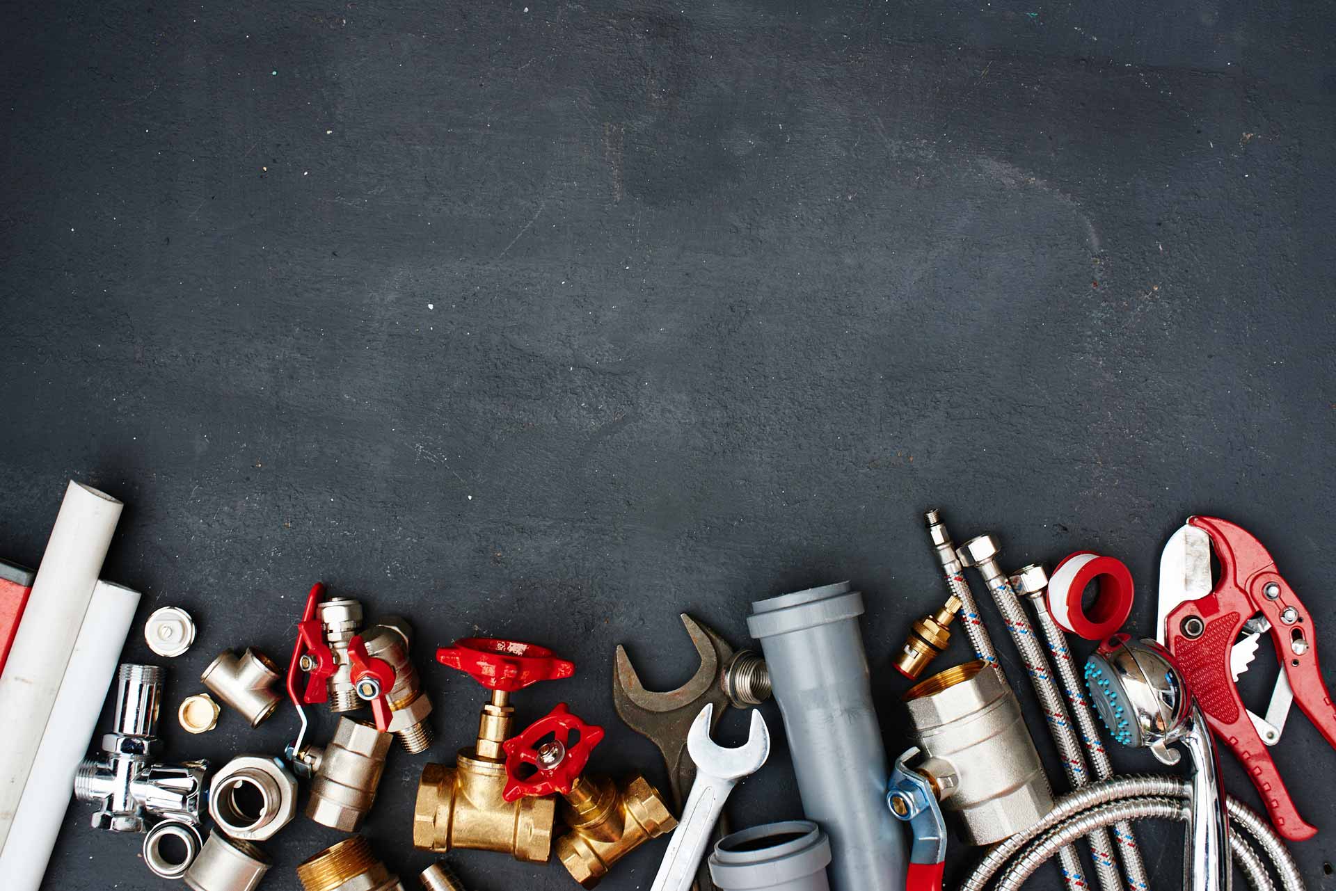 Wrenches and various plumbing supplies scattered on black background