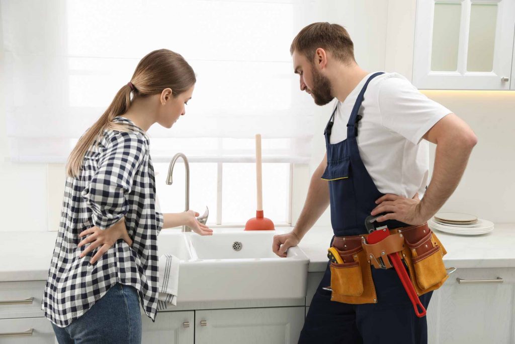 Homeowner explains problem to plumber as both look over kitchen sink